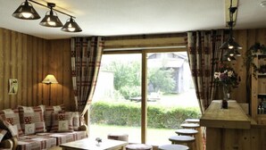 Una habitación acogedora con detalles de madera, un conjunto de sofás, una mesa de comedor y una zona de bar con taburetes.