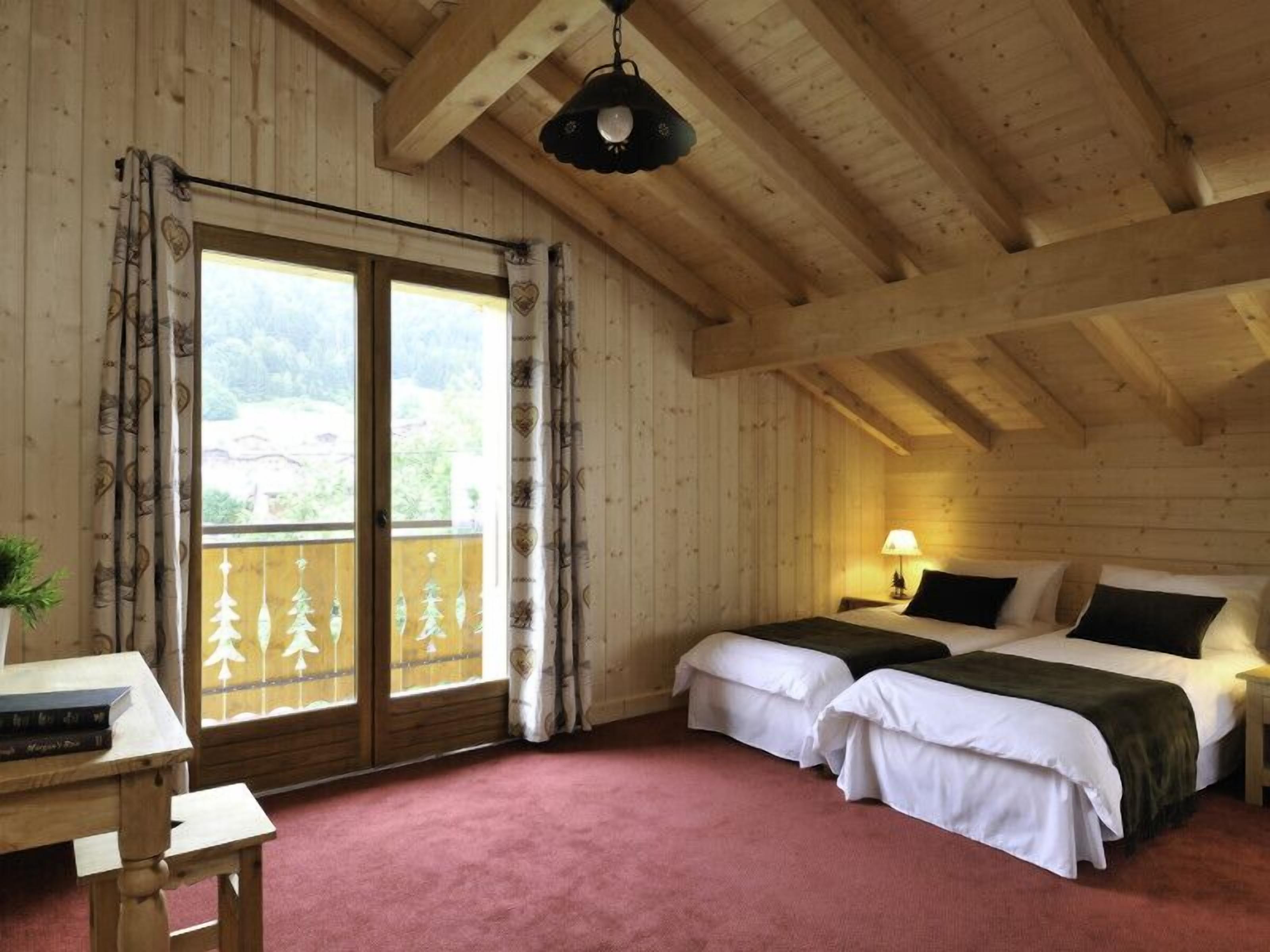 A wooden cabin room with two beds, a table, and a window with curtains.