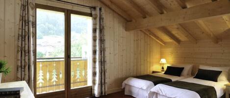 A wooden cabin room with two beds, a table, and a window with curtains.