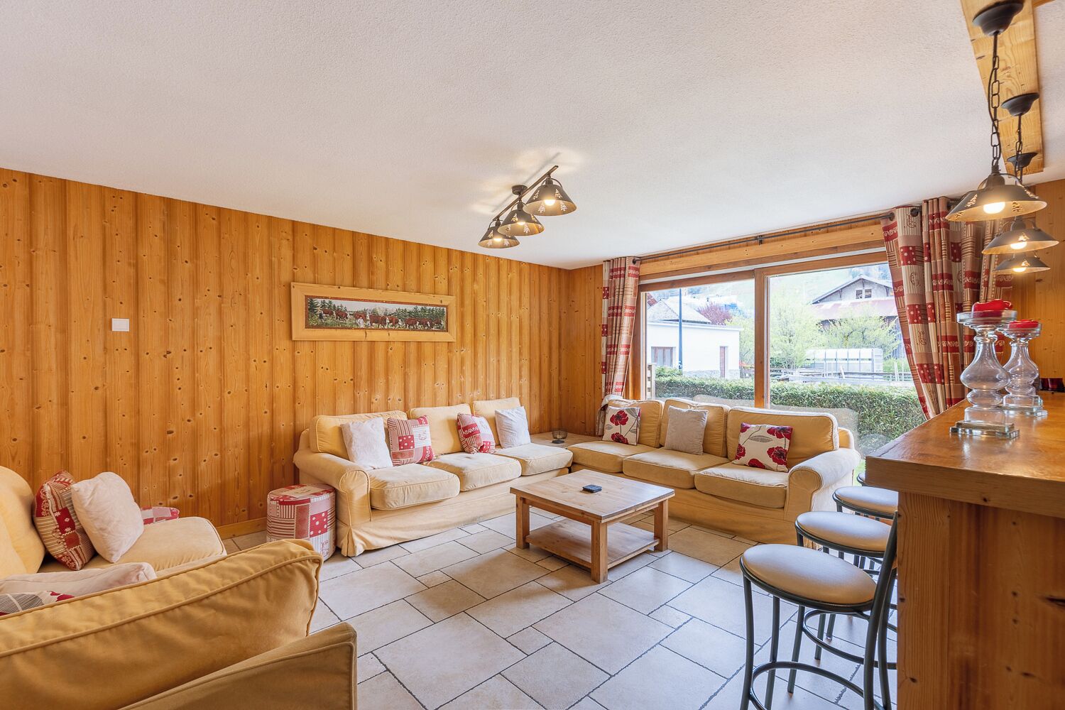 A cozy living room with wooden walls, a sofa set, a coffee table, and a bar area with stools.