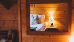 Una habitación de cabaña acogedora, con interior de madera, una cama con ropa blanca y una pequeña mesita de noche con una lámpara.