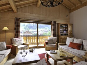 A cozy room with wooden walls and a large window offering a view of a village. There are two sofas, a table with candles, and a bookshelf. - Savoy Morzine (Morzine)