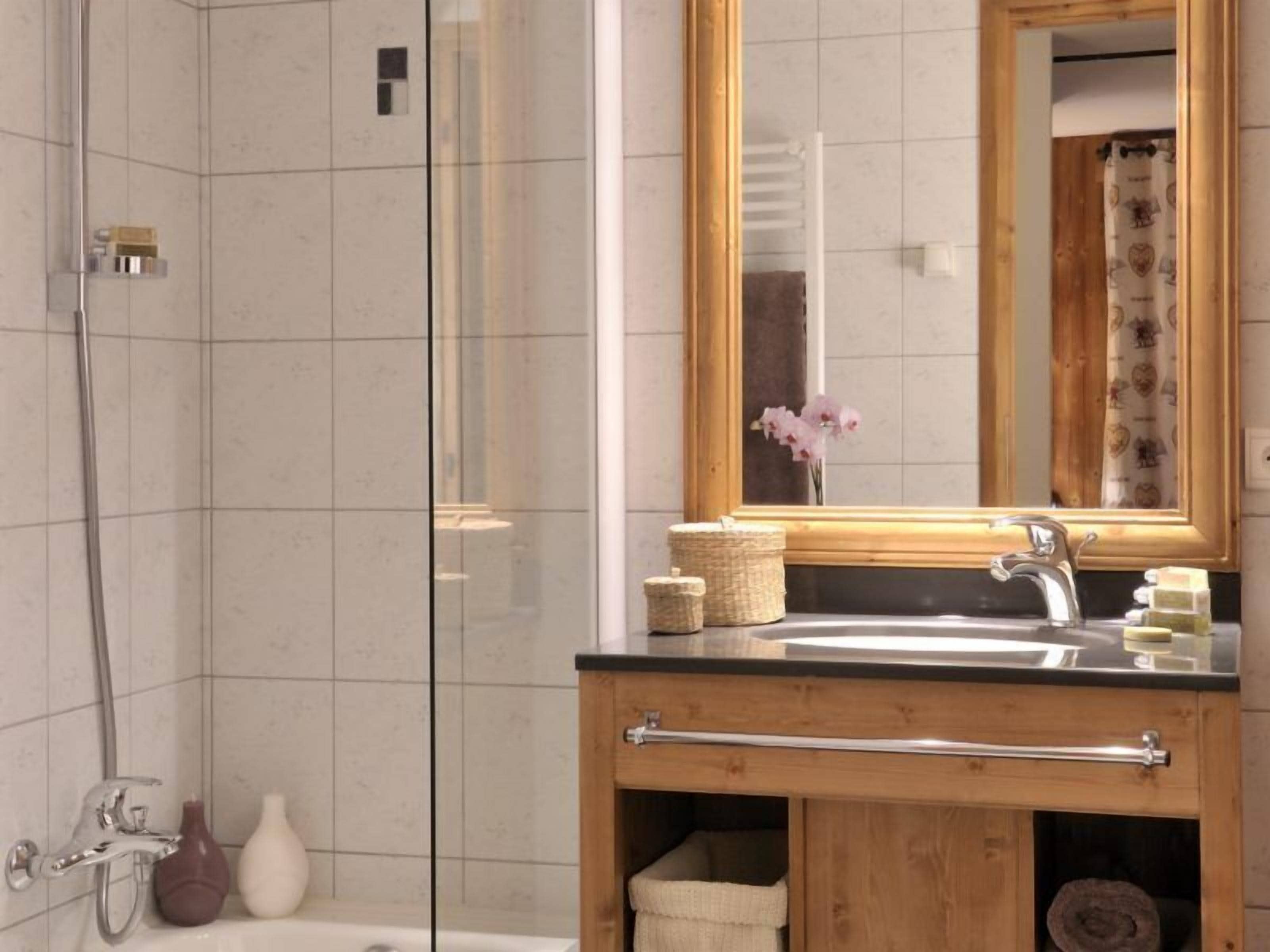 Un baño moderno con cabina de ducha de vidrio, un mueble de tocador de madera con lavamanos y un espejo.