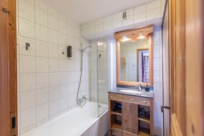 A bathroom with a glass-enclosed shower, a white bathtub, and a wooden vanity with a mirror. - Savoy Morzine (Morzine)
