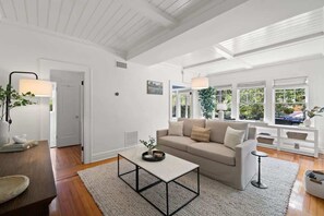 Ein geräumiges Wohnzimmer mit einem beigen Sofa, einem Couchtisch und Blick auf Grün durch große Fenster.