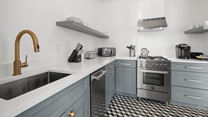 Una cocina moderna con estufa de acero inoxidable, horno empotrado, microondas y lavamanos con grifo dorado.