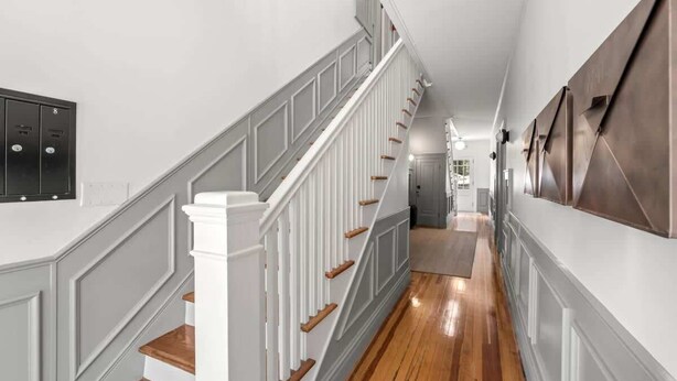 A hallway with a wooden floor, white walls, and a staircase with white railings and wooden steps.
