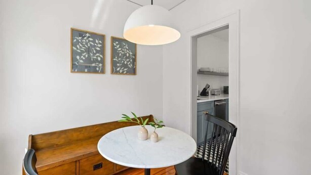 Un comedor con una mesa redonda, dos plantas en macetas, un banco y una silla negra.