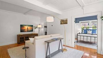 Un salon avec un canapé blanc, une petite table, un lampadaire et un tableau accroché au mur.