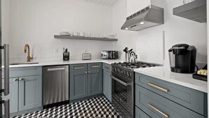 Eine moderne Küche mit grauen Schränken, einem schwarz-weißen Schachbrettfußboden, einem Einbauofen, einer Kaffeemaschine und einer Mikrowelle.