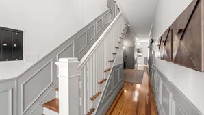 Ein Korridor mit Holzboden, weißen Wänden und einer Treppe mit weißen Geländern und Holzhinweisstufen.