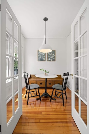 Un comedor con una mesa redonda, dos sillas, una lámpara colgante y un cuadro en la pared.