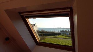 A skylight with a view of a body of water, a grassy area, and a distant building. - House near Presses beach in Saint Philibert (Saint-Philibert)