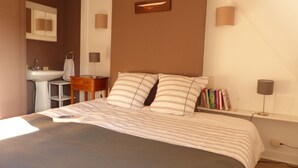 A bedroom with a bed, bedside lamps, a nightstand, a bookshelf, and a bathroom with a sink and mirror. - House near Presses beach in Saint Philibert (Saint-Philibert)