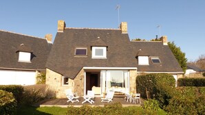 A two-story house with a sloped roof, a front porch with white chairs, and a small garden area. - House near Presses beach in Saint Philibert (Saint-Philibert)