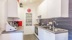 Een moderne keuken met witte kasten, een zwarte spatwand en een waterkoker op het aanrecht.