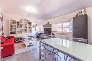 Een moderne woonkamer met een rode bank, een glazen salontafel en een keuken met witte kasten en een donkere koelkast.