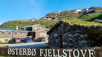 A wooden sign with the text "ØSTERBO Fjellstove" in front of a building with a green roof and a stone structure to the right.