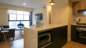 A modern kitchen with a central island, built-in oven, and a dining area with a blue chair and a small table. - w* | Art Deco 1BR in Barranco (Barranco)