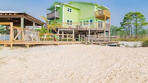 A beachfront property with a two-story house, wooden deck, and a covered area. - Sandcastle 6A Completely Renovated Modern Condo On the Water Steps to the Beach (Dauphin Island)