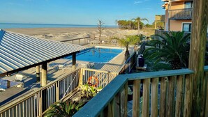 A pool area with a view of the beach, wooden deck, and a building with balconies. - Sandcastle 6A Completely Renovated Modern Condo On the Water Steps to the Beach (Dauphin Island)