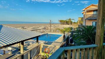 Un espace piscine avec vue sur la plage, une terrasse en bois et un bâtiment doté de balcons.