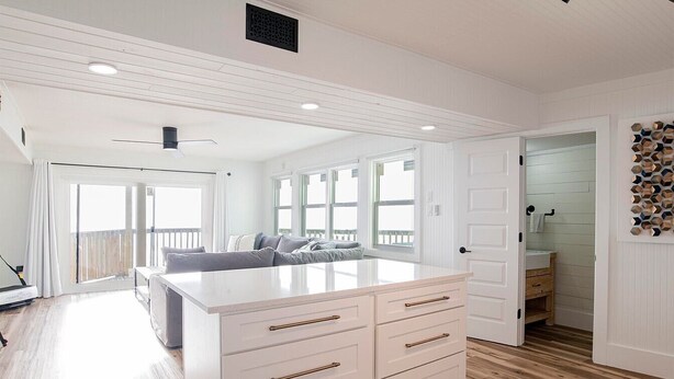A spacious living area with a large white island, a sofa, and a view to the outside. - Sandcastle 6A Completely Renovated Modern Condo On the Water Steps to the Beach (Dauphin Island)