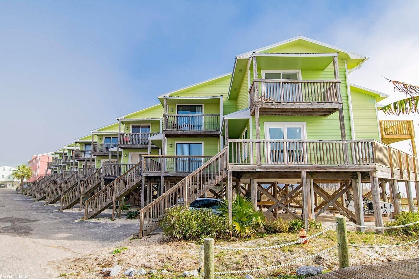 A row of multi-story beachfront buildings with wooden balconies and staircases leading to the ground level.