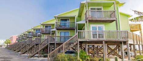 A row of multi-story beachfront buildings with wooden balconies and staircases leading to the ground level.