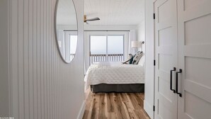 A bedroom with a large bed, a ceiling fan, a window with a view, and a door with a handle. - Sandcastle 6A Completely Renovated Modern Condo On the Water Steps to the Beach (Dauphin Island)