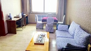A living room with a sofa, a coffee table with decorative items, a desk with a chair, and a large window with curtains. - Nancha Hotel (Nancha County)
