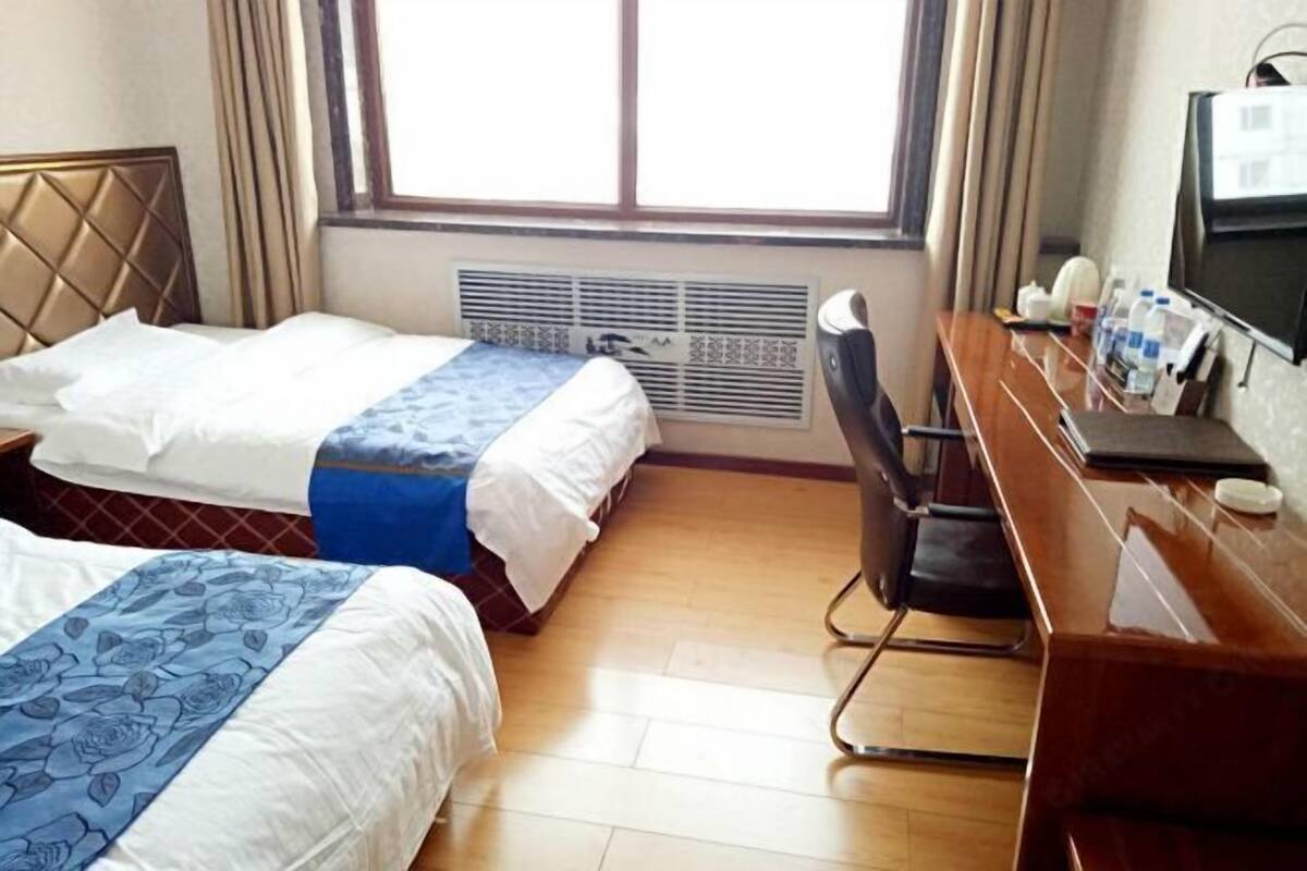 Hotellihuone, jossa on kaksi sänkyä, työpöytä ja tuoli, televisio sekä ikkuna, jossa on verhot.