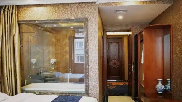 A hotel room with a large bed, a glass-enclosed shower, and a wooden wardrobe. - Nancha Hotel (Nancha County)