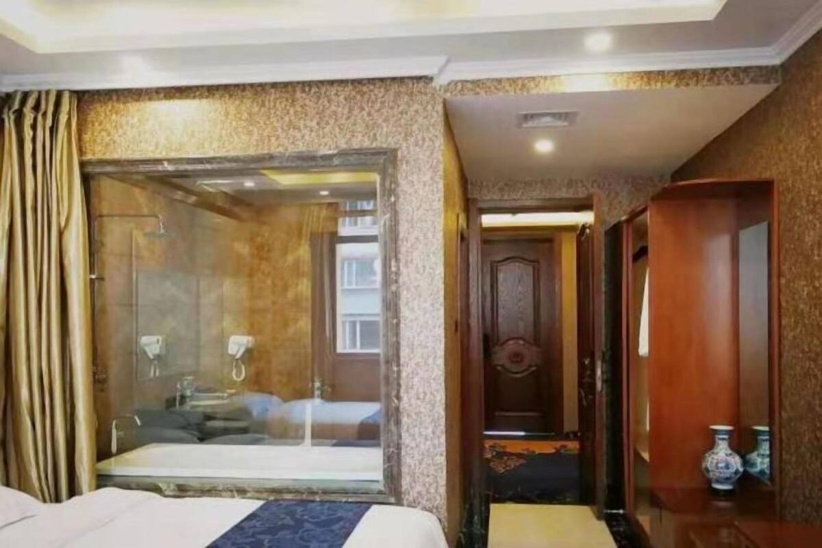 Hotellihuone, jossa on suuri sänky, lasiseinällinen suihku ja puinen vaatekaappi.