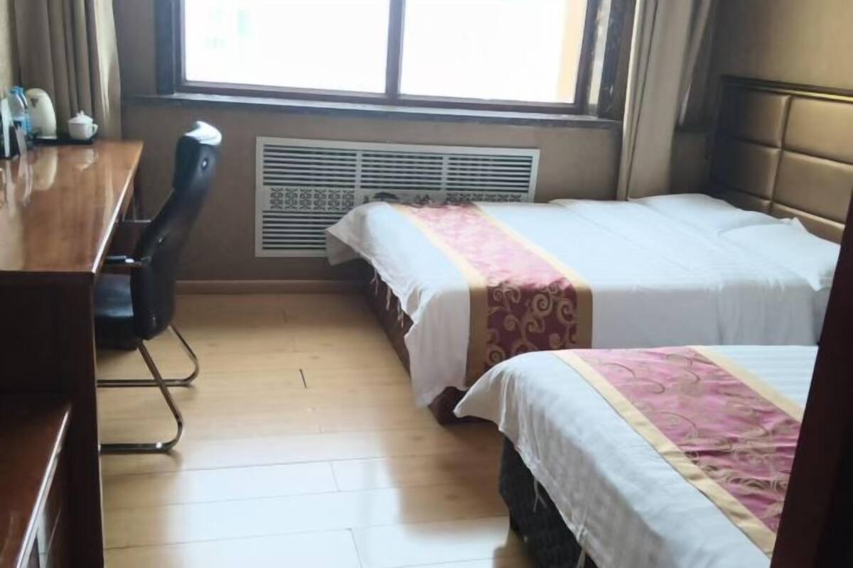 Hotellihuone, jossa on kaksi sänkyä, puinen työpöytä, tuoli ja ikkuna, josta on näkymä.