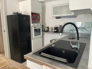 Uma cozinha compacta com geladeira preta, forno embutido, micro-ondas e pia de aço inoxidável.