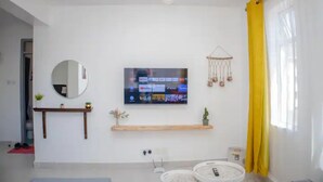 Ett modernt vardagsrum med en platt-TV som är monterad på väggen, en trähylla under den, en rund spegel och en hängande växt.