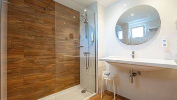 Un baño moderno con ducha de vidrio, un lavamanos blanco y un espejo redondo.