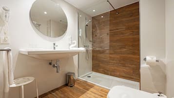 A modern bathroom with a round mirror, white sink, and a glass-enclosed shower.