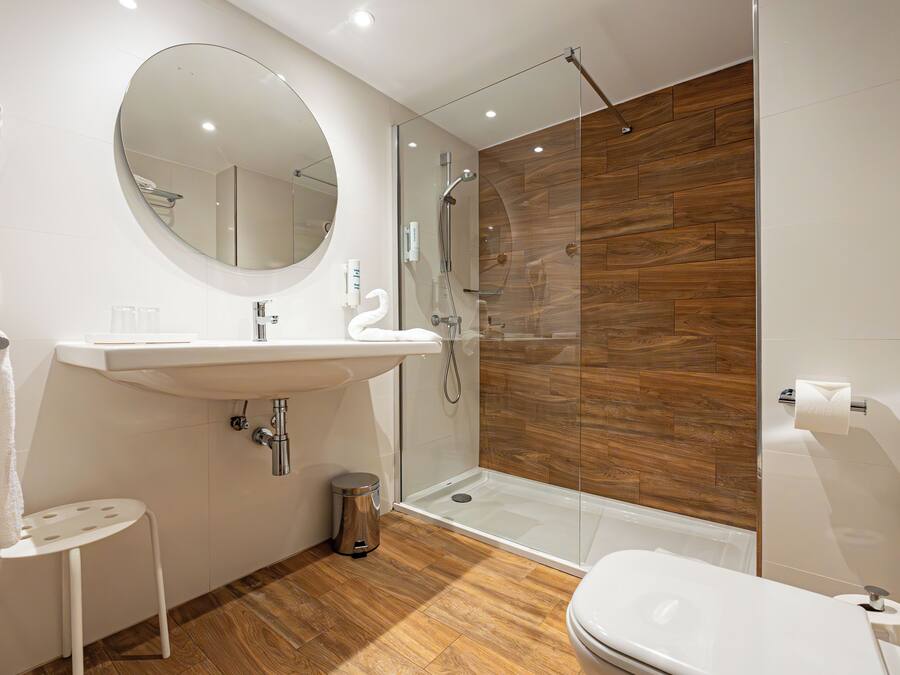 A modern bathroom with a round mirror, white sink, and a glass-enclosed shower.