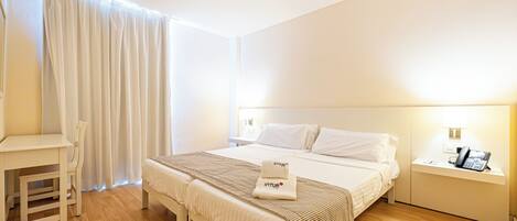 Una camera d'albergo con un letto, un comodino e una scrivania con una sedia.