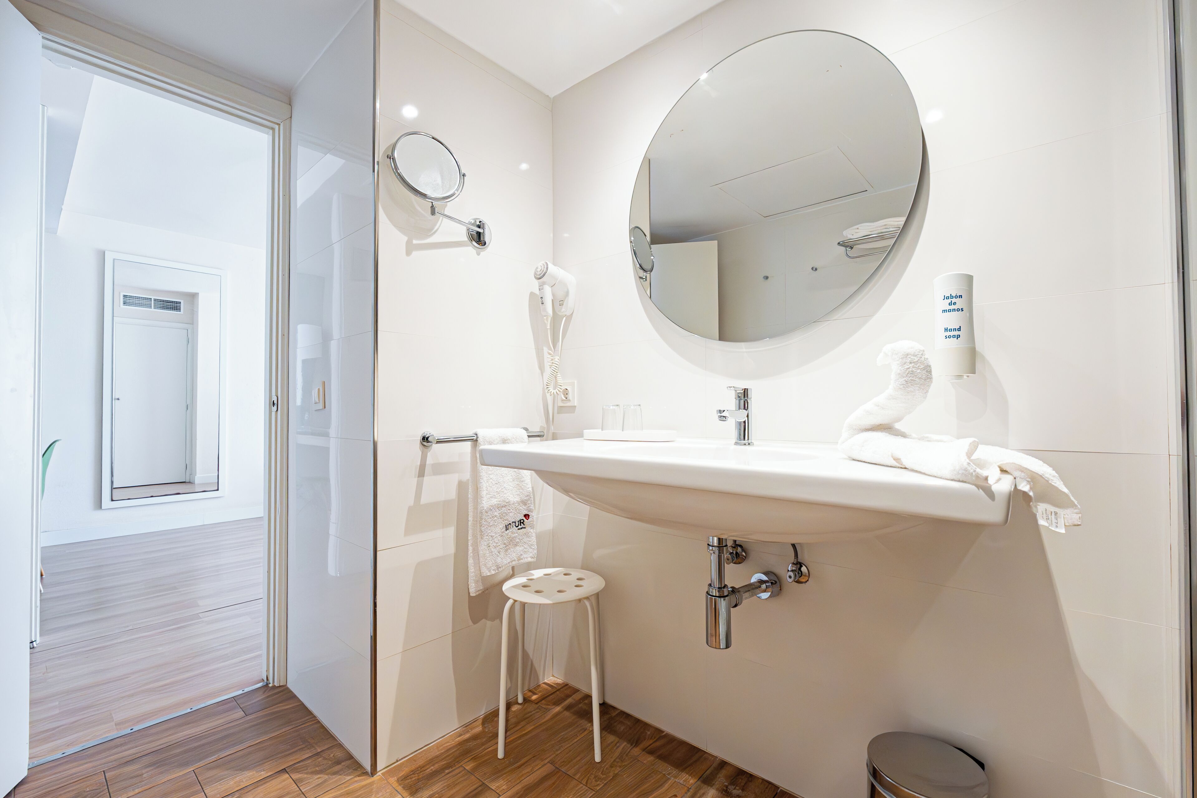 A modern bathroom with a large sink, a round mirror, a hairdryer, and a toilet.