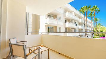 Un balcón con una mesa y sillas, con vistas a un edificio con varios balcones y palmeras.