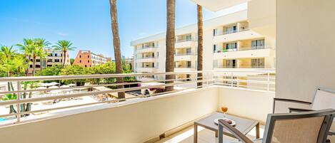 Un balcon avec une table et des chaises, donnant sur une piscine et des palmiers.