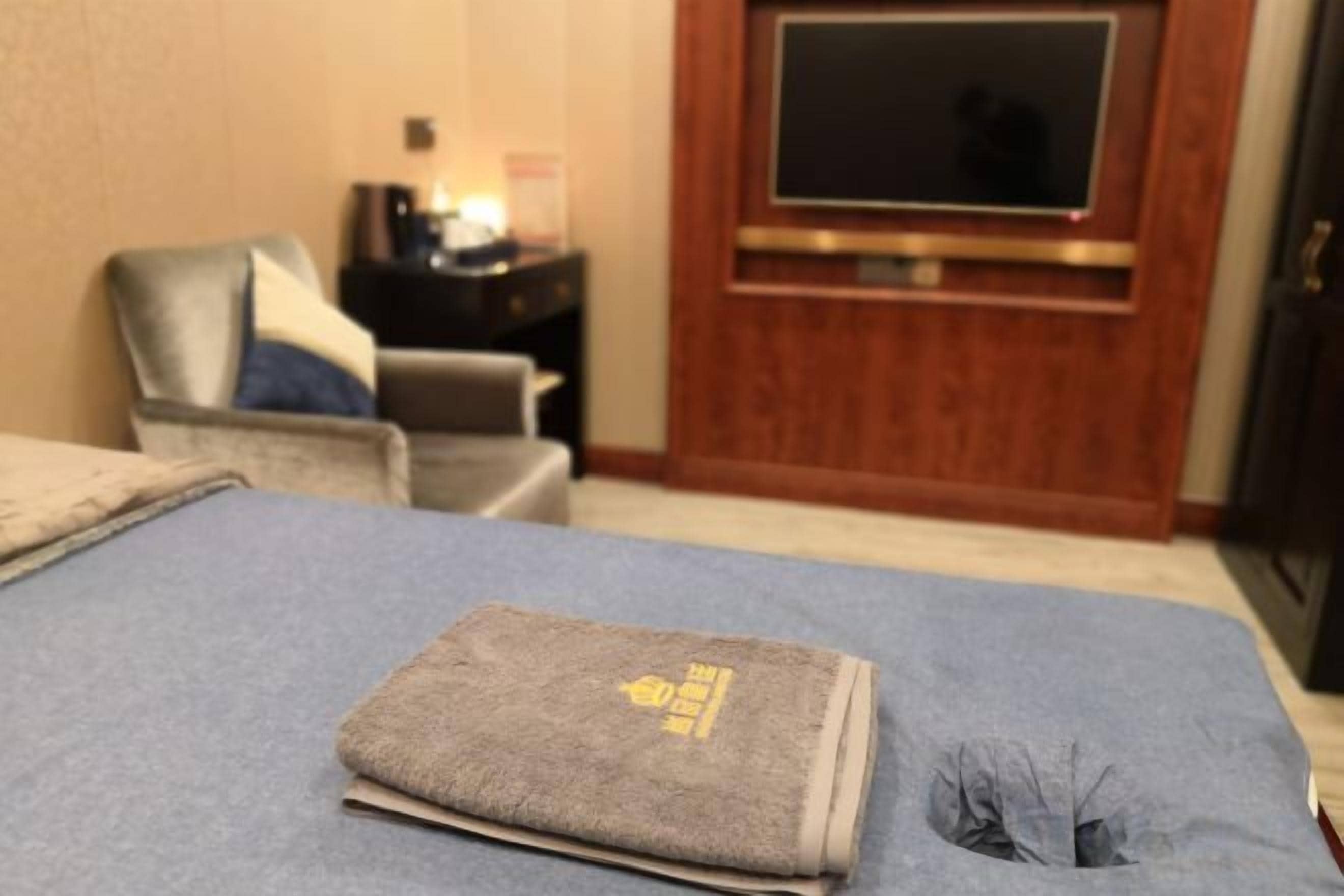 A hotel room with a bed, a television, a nightstand, and a seating area with a chair and a small table.