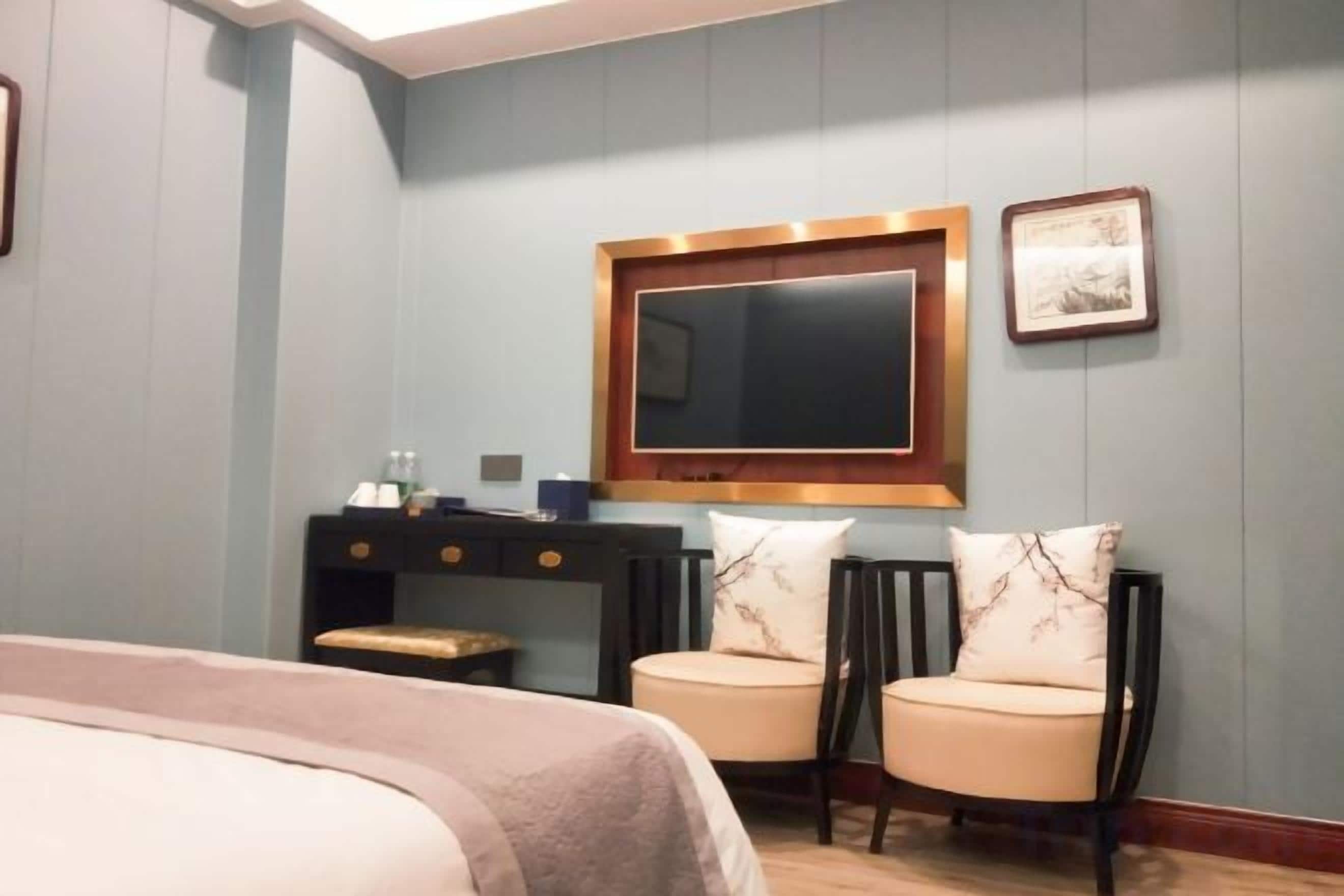 Une chambre d’hôtel avec un lit, un bureau et une chaise, une télévision et un tableau encadré au mur.