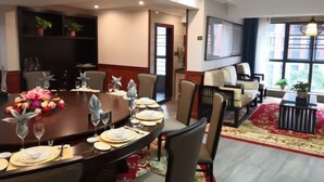 A dining area with a round table set for a meal, surrounded by chairs. There is a bookshelf with plants on the wall, a large window with a view, and a red carpet on the floor. - Shangpin Huangting Kangyang Hotel (Ningxiang)