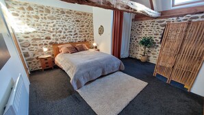 Une chambre avec un mur en pierre, un cadre de lit en bois, une table de chevet avec une lampe, un grand tapis et un paravent en bambou.