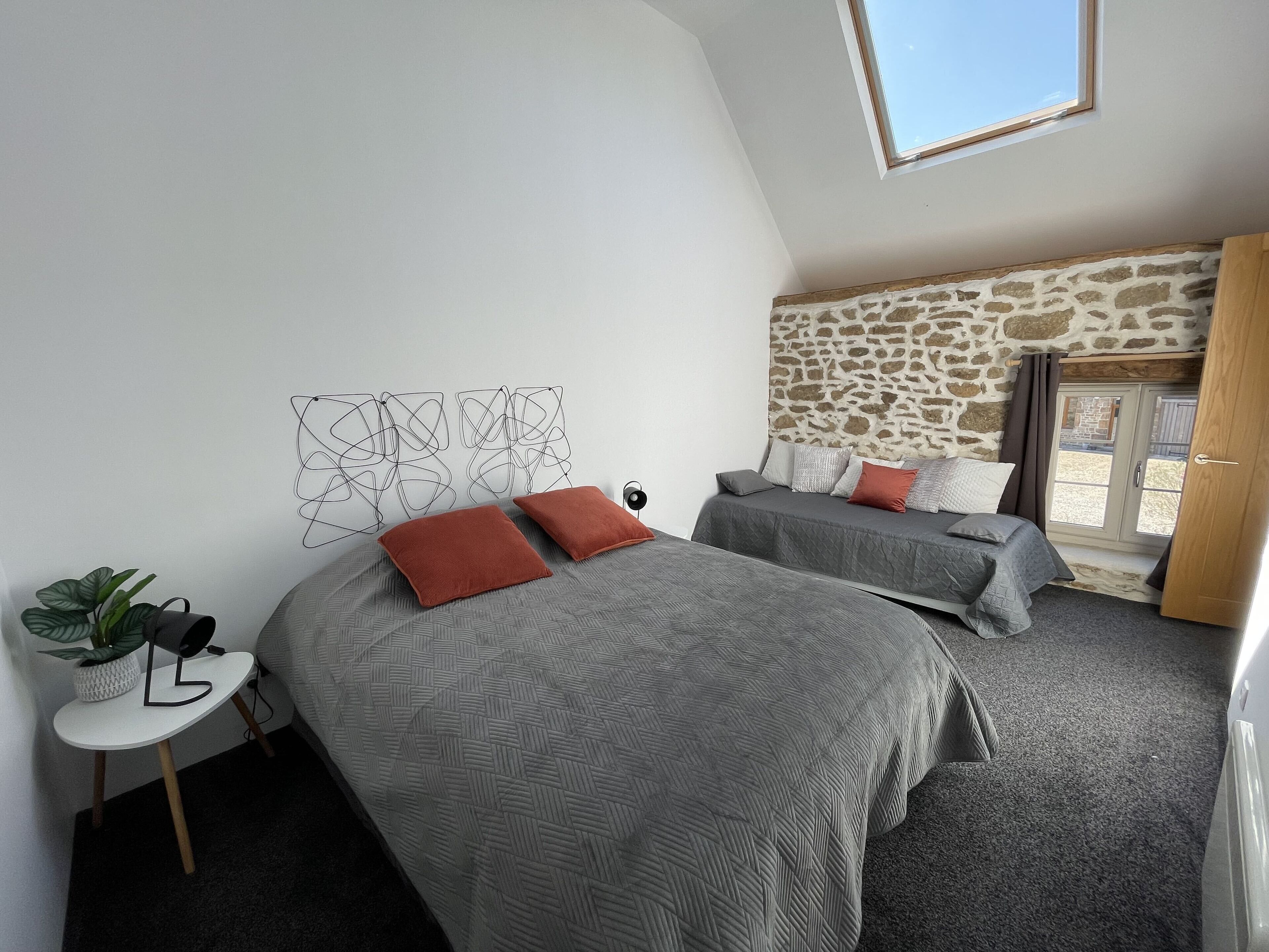 A modern bedroom with two beds, a small table with a plant, and a stone wall.