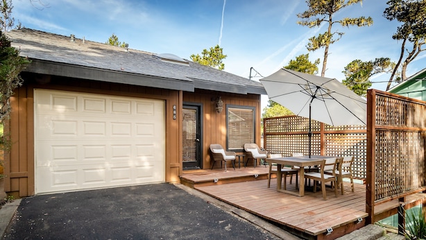 En garage med en hvid dør, en lille veranda med et bord og stole, samt en træterrasse.